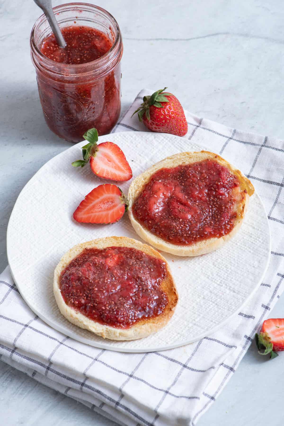 Two english muffins on white plate with strawberry chia jam on top
