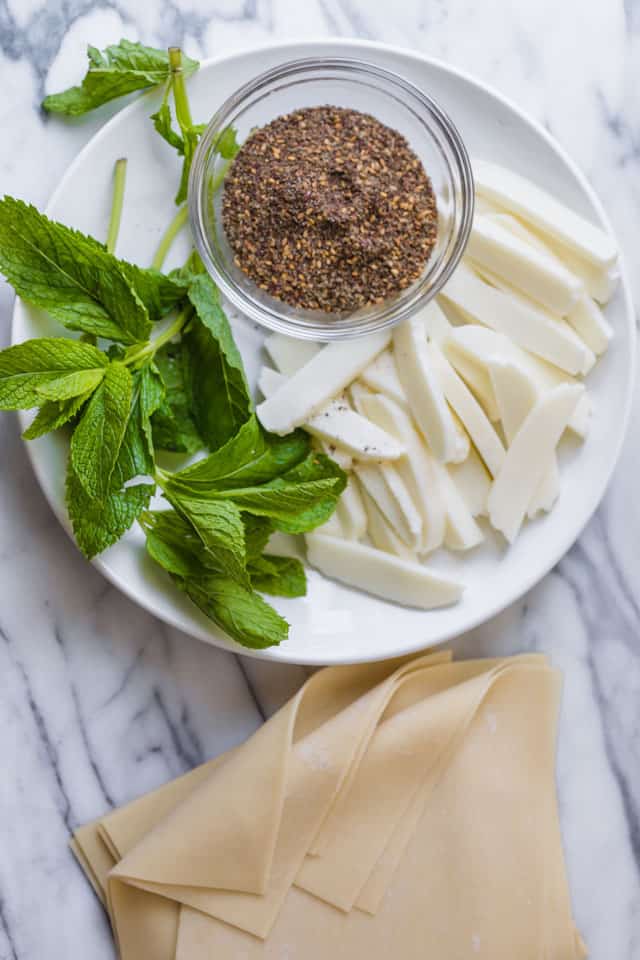 Plate with halloumi cheese, mint leaves, zaatar and wonton wrappers to make zaatar spring rolls