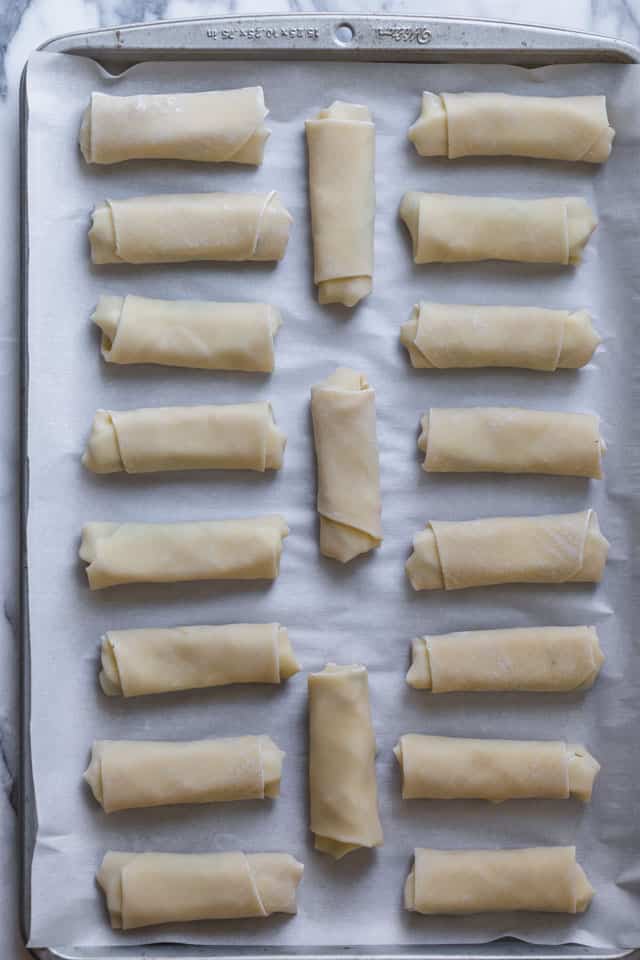 Baking tray with parchment paper showing zaatar spring rolls all rolled up
