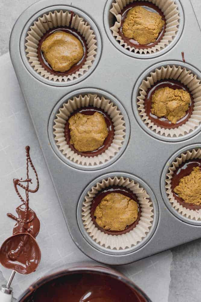 Lined mini cupcake tin with a layer of melted chocolate followed by pistachio butter.