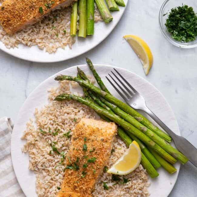 Two plates of Panko Crusted Salmon with asparagus over brown rice with lemon wedges