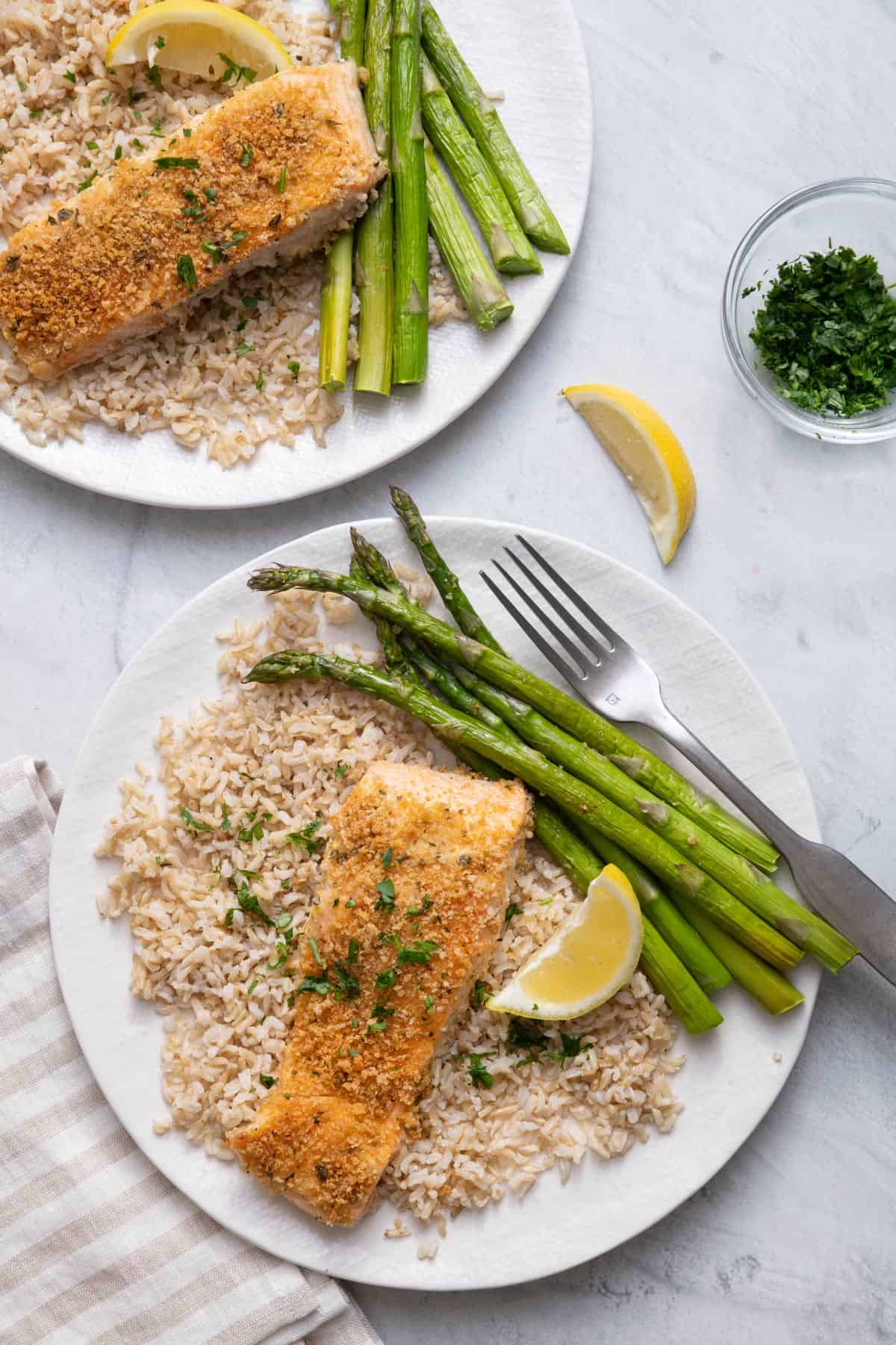 Two plates of Panko Crusted Salmon with asparagus over brown rice with lemon wedges
