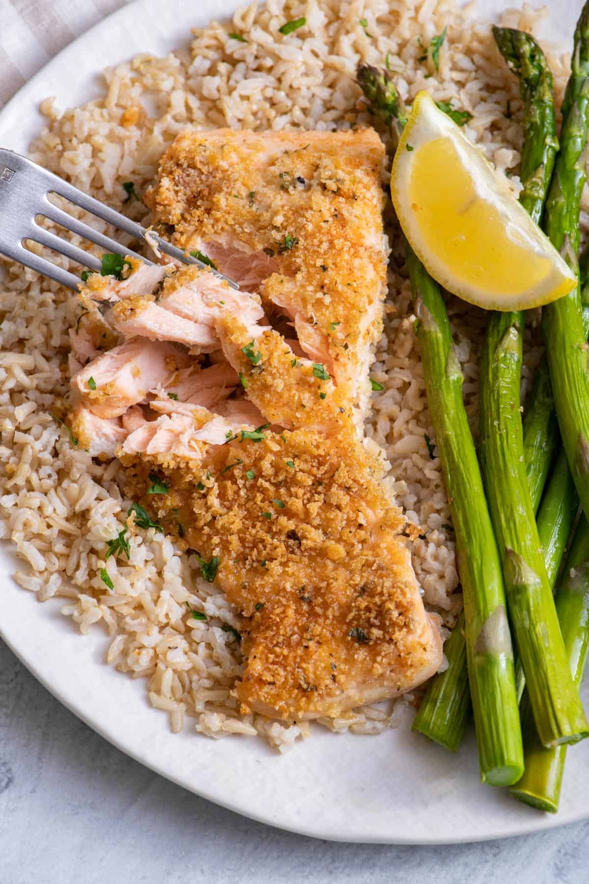 Panko Crusted Salmon on a white plate over brown rice with fork removing piece from salmon