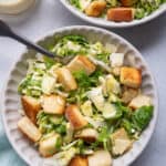 Two small bowls of the brussel sprout salad with croutons and dressing on the side