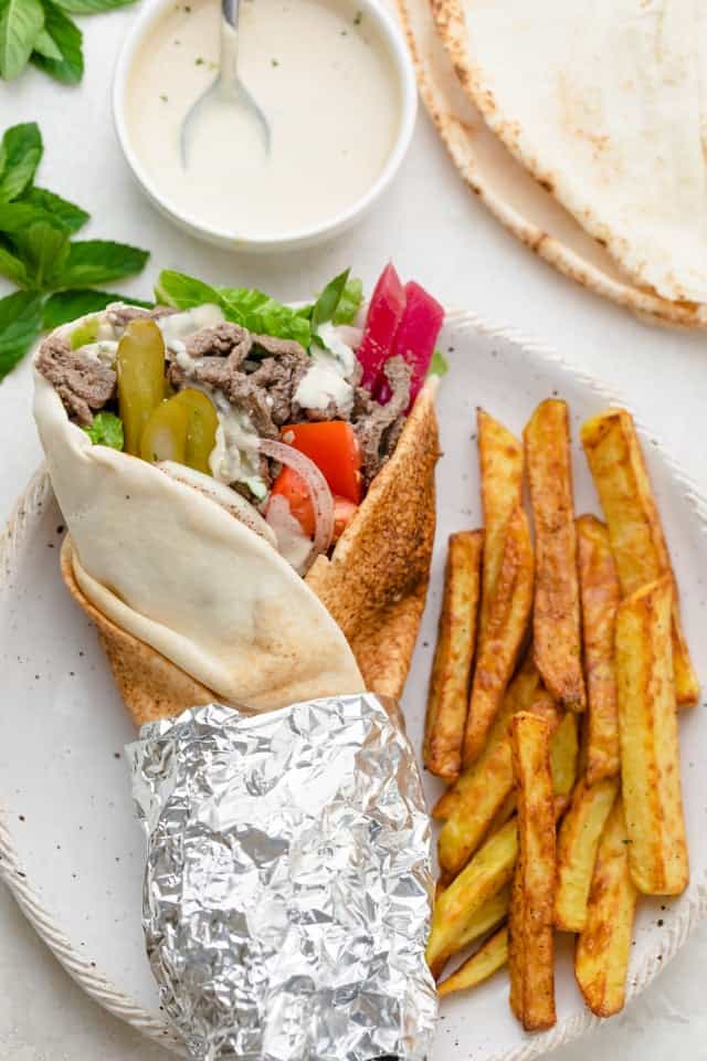 Beef shawarma wrap rolled up in a pita bread, alongside french fries