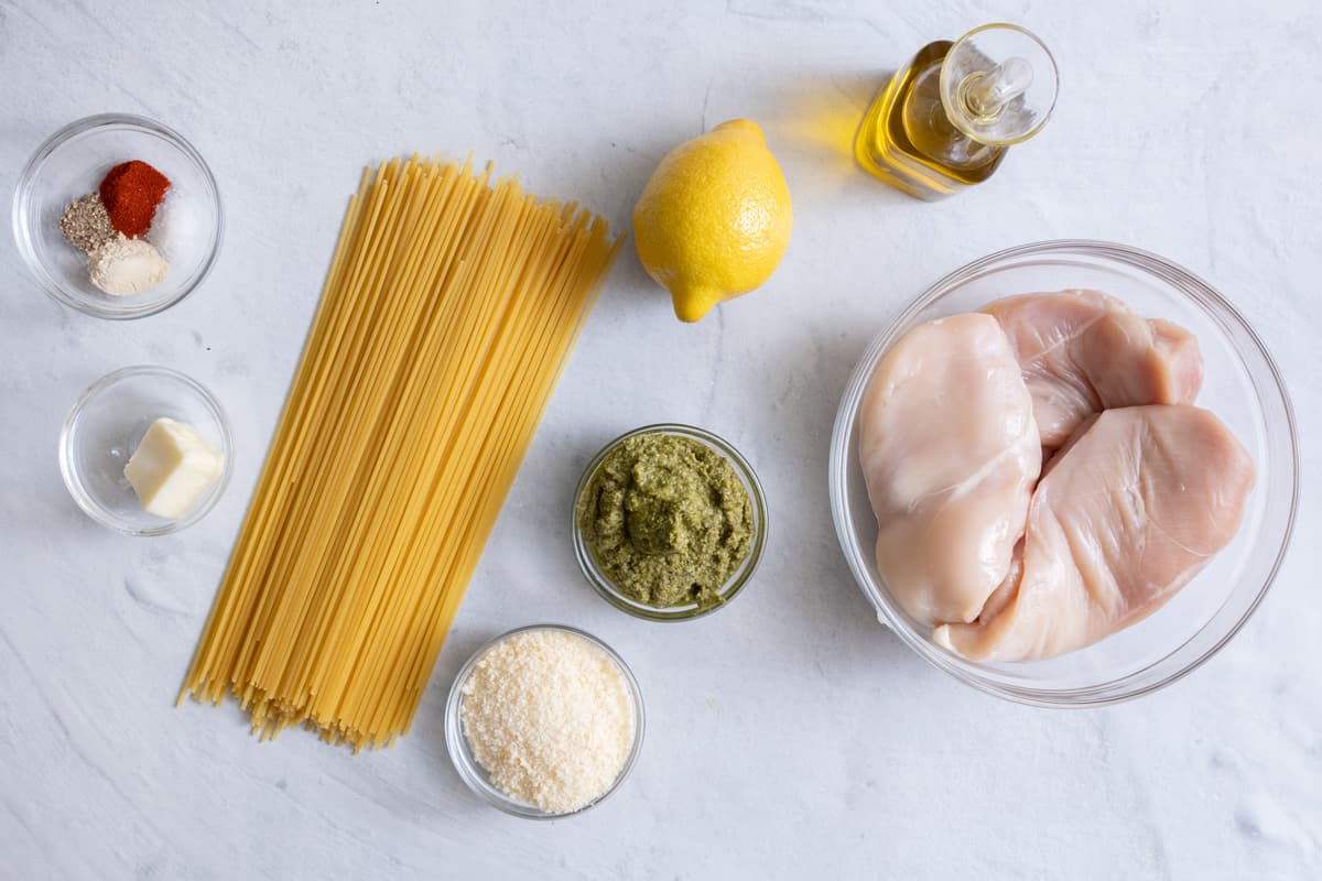 Ingredients for the recipe before being prepped: spices, butter, dry pasta, Parmesan cheese, pesto, lemon, oil, and raw chicken.