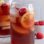 Two tall glasses of Raspberry Iced Tea lemon slices and fresh raspberries and a small white dish of raspberries.