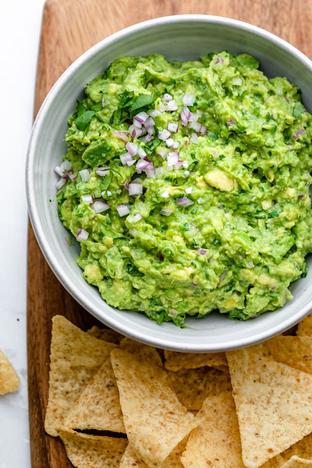 Guacamole recipe in a large bowl with chips on cutting board