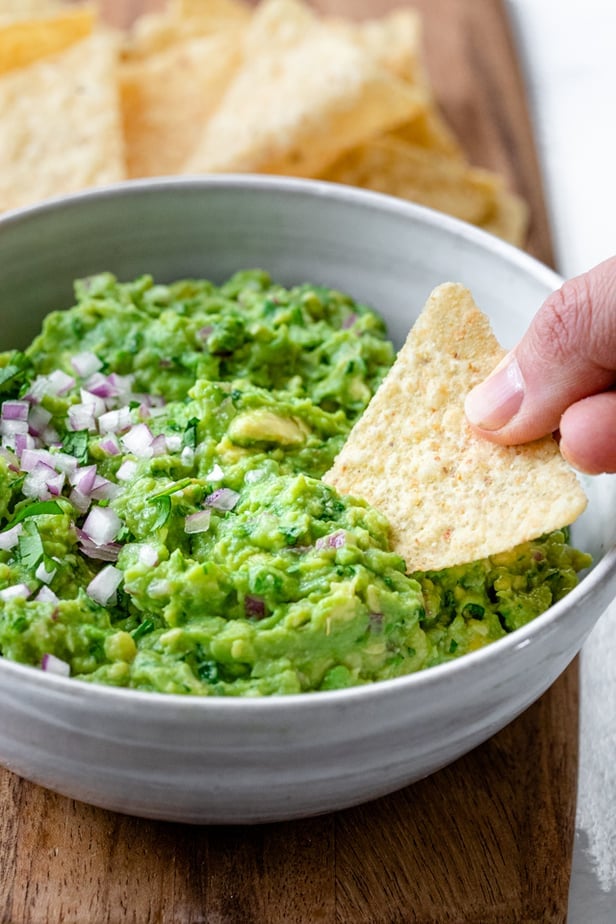 Hand holding tortilla chip and dipping into bowl of guac