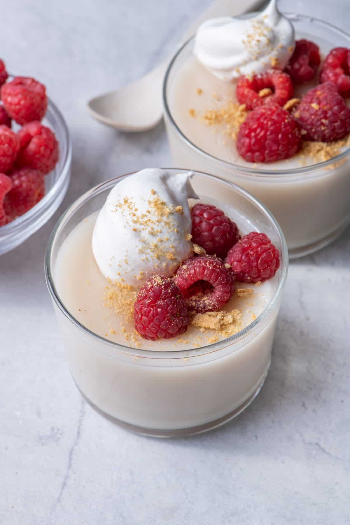 Vegan pudding in glass jars topped with raspberries and whipped cream