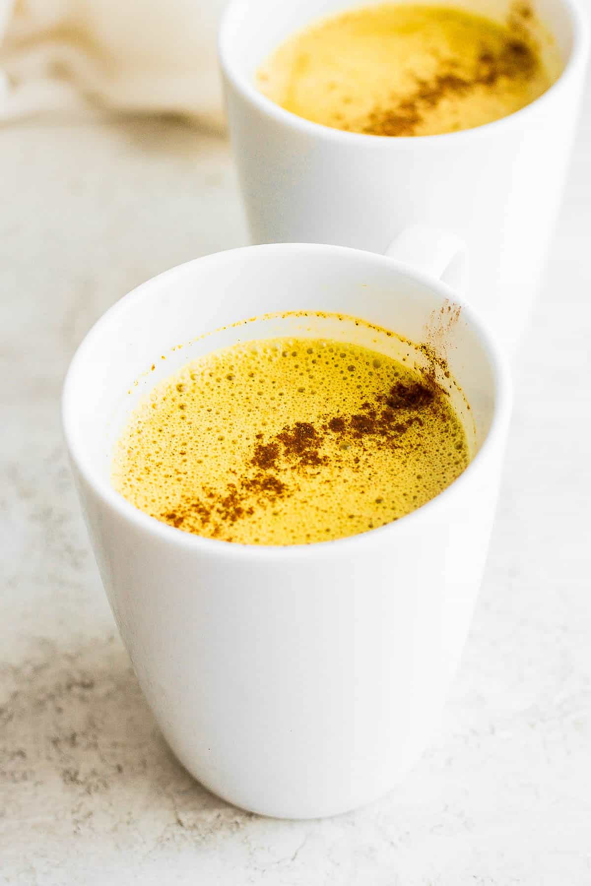 Two mugs of golden milk turmeric latte with spices on top