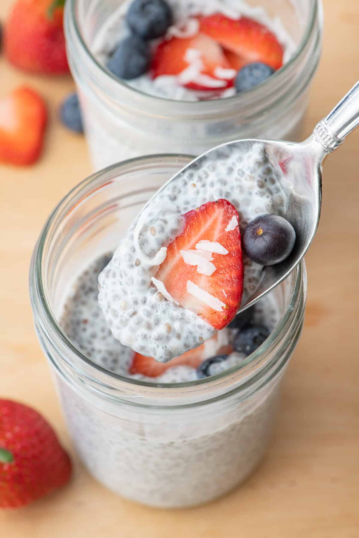 3 ingredient chia seed pudding with berries on top and a spoon scooping some up to show pudding like consistency.