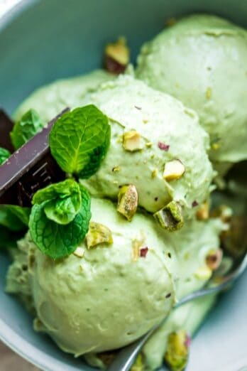 Three scoops of avocado ice cream in a bowl with garnish and a spoon.