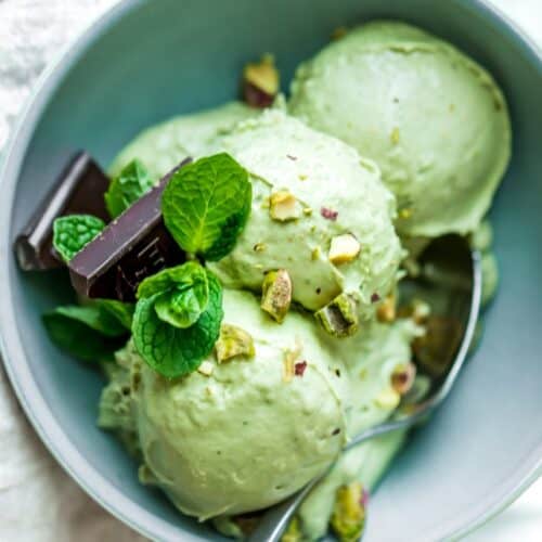 Three scoops of avocado ice cream in a bowl with garnish and a spoon.