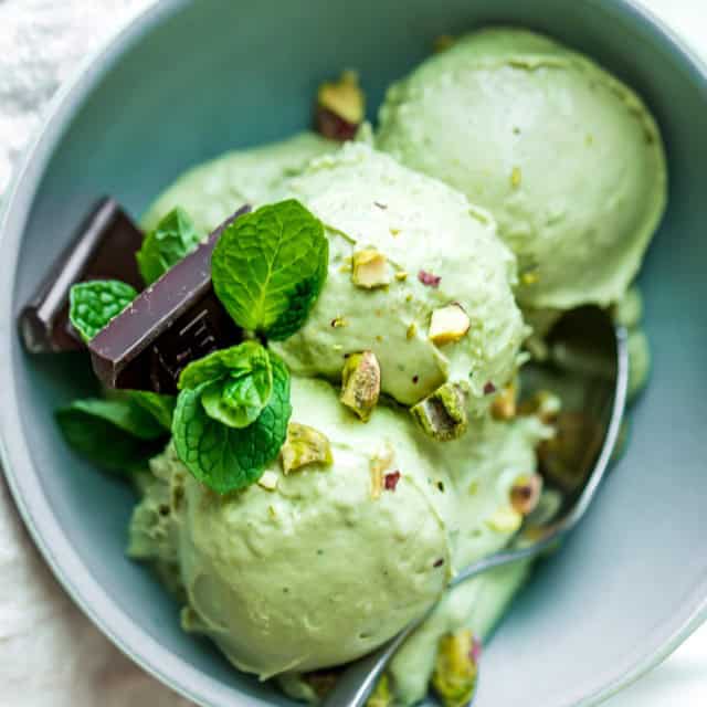 Three scoops of avocado ice cream in a bowl with garnish and a spoon.