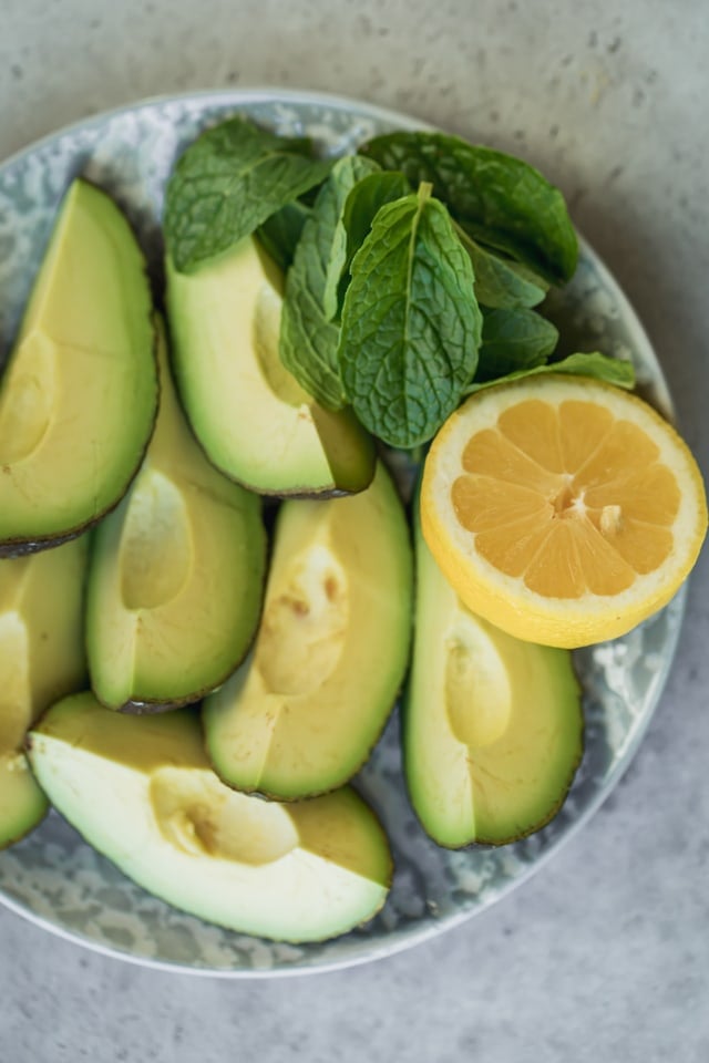 Plate of ripe avocados cut into quarters, with half a lemon and mint leaves