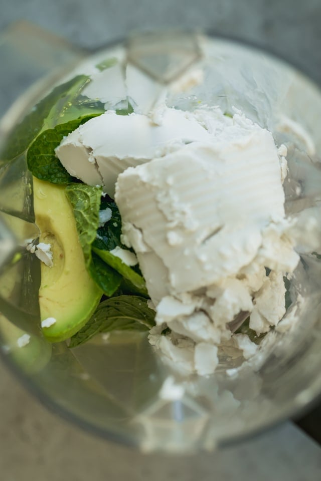 Top view of blender with avocados, coconut milk, mint leaves, maple syrup, lemon juice and bananas underneath - the making of avocado ice cream