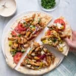 Lebanese style chicken shawarma pita pizza cut into four parts on a plate with hand grabbing one slice