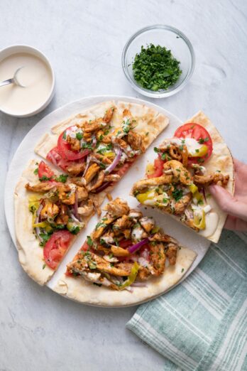 Lebanese style chicken shawarma pita pizza cut into four parts on a plate with hand grabbing one slice
