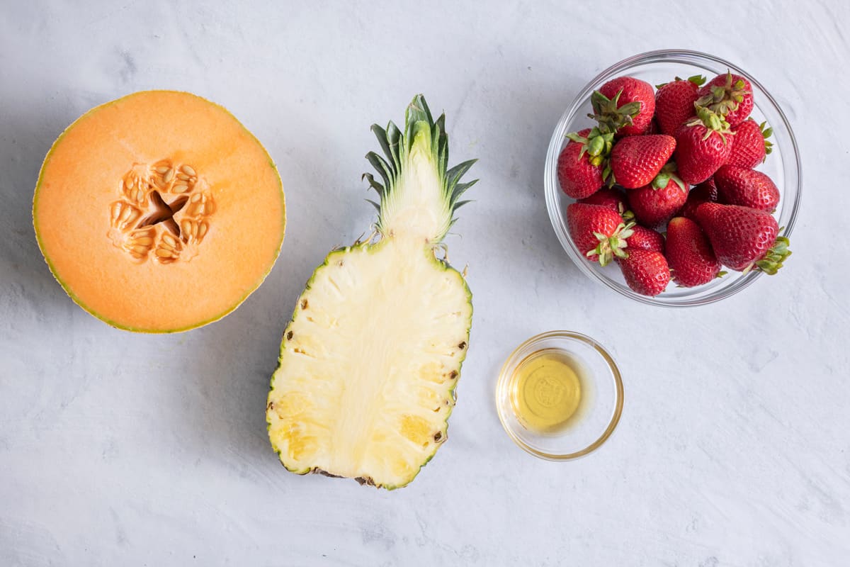 Ingredients for fruit skewer recipe: half cantaloupe, half pineapples, whole strawberries, and lemon juice.