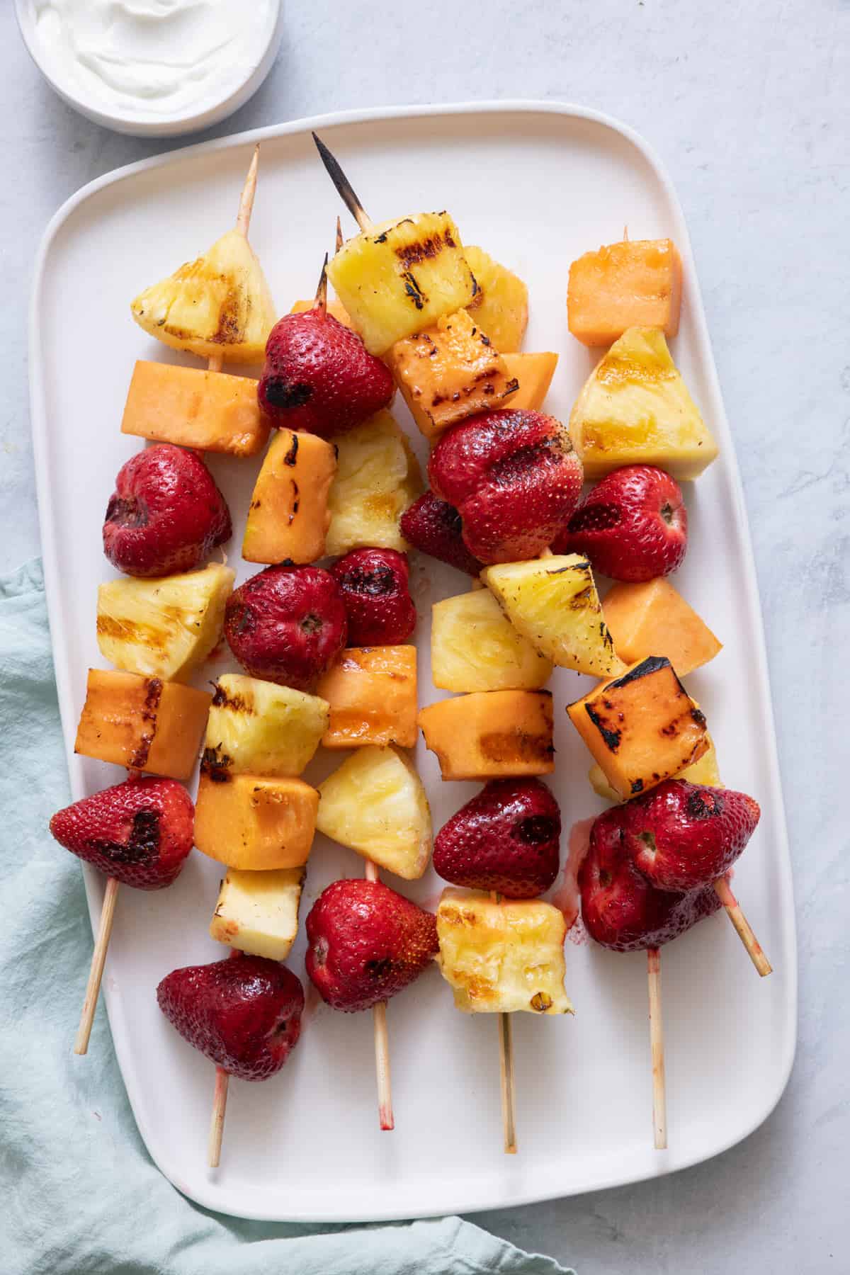 Large rectangle white platter with 6 Grilled fruit kabobs.