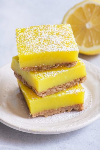 Stack of three vegan lemon bars on small white dish with half lemon in background