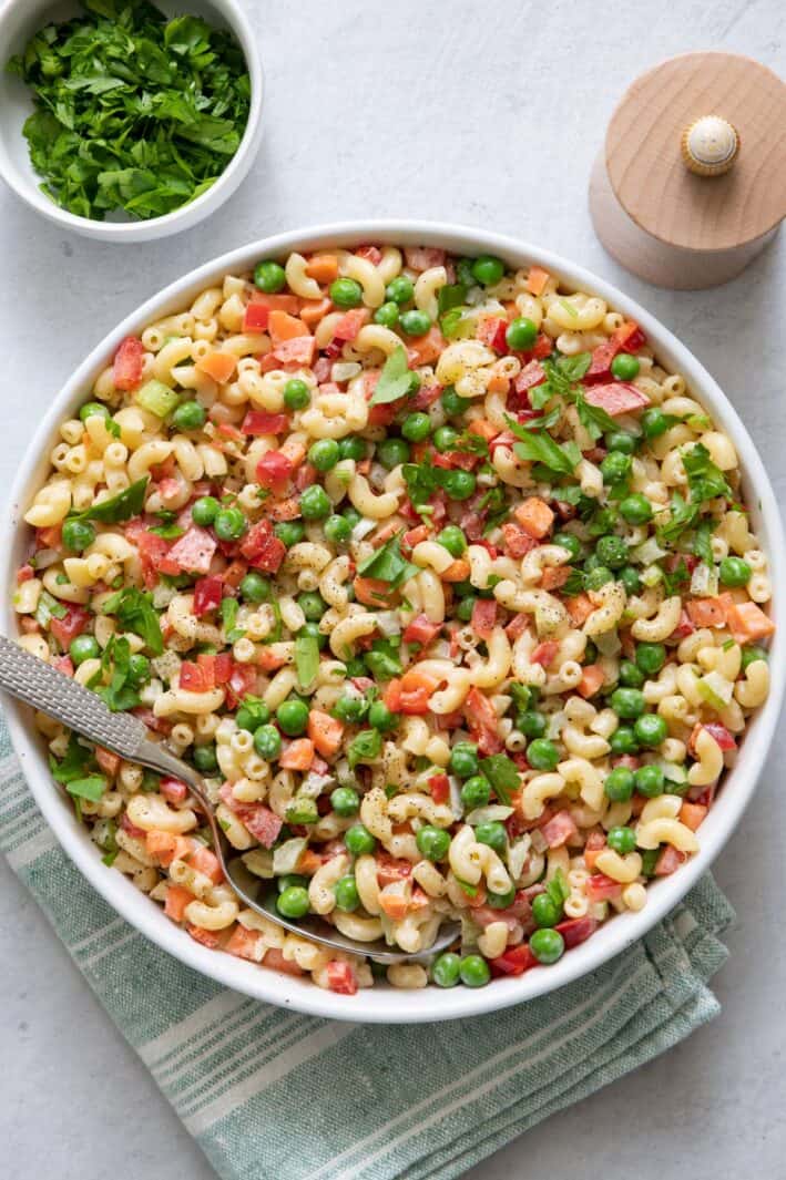 Large bowl of Vegan Macaroni Salad with pasta, peas, carrots, celery, red pepper, tossed in dressing.