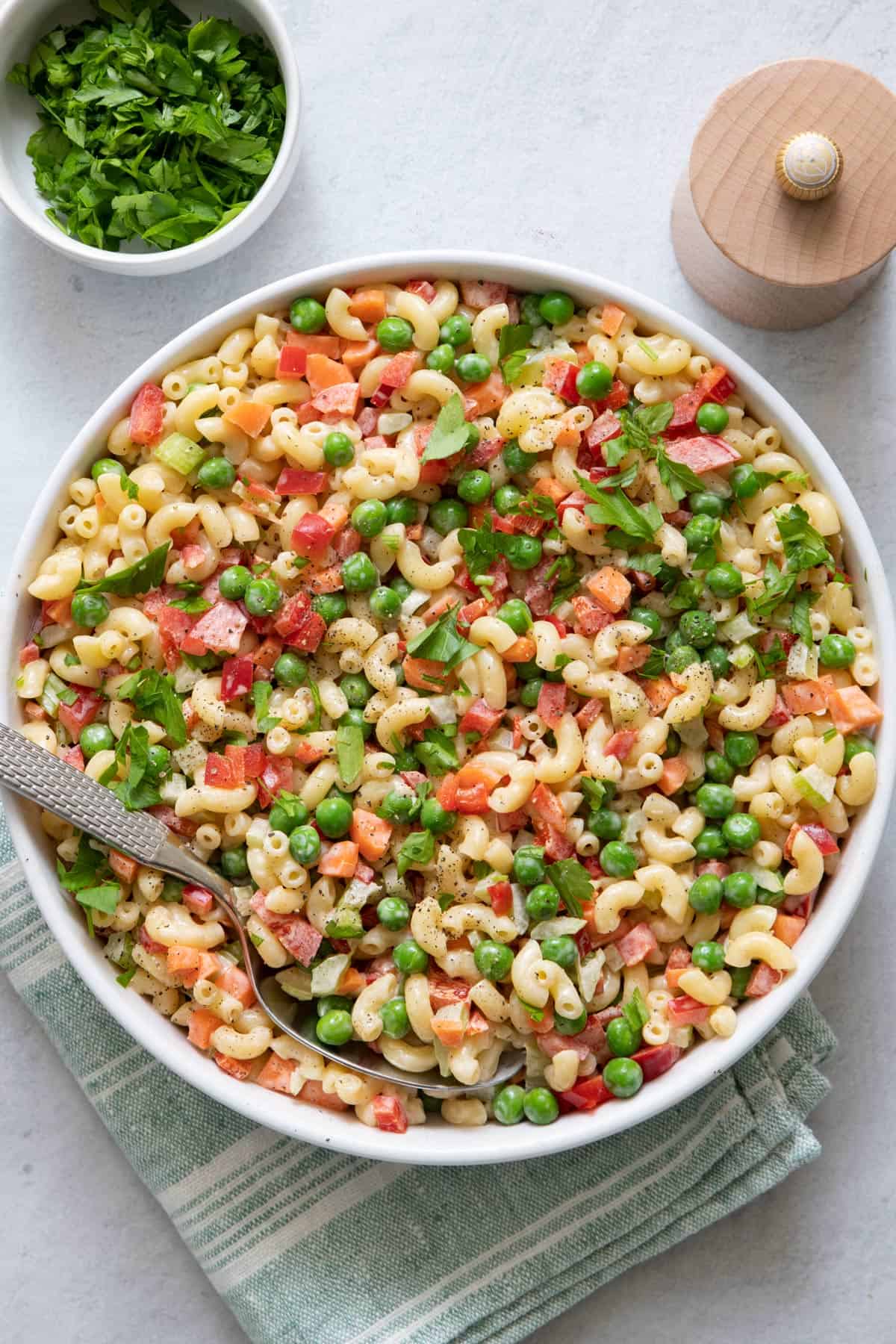 Large bowl of vegan macaroni salad with pasta, peas, carrots, celery, red bell pepper, tossed in dressing.