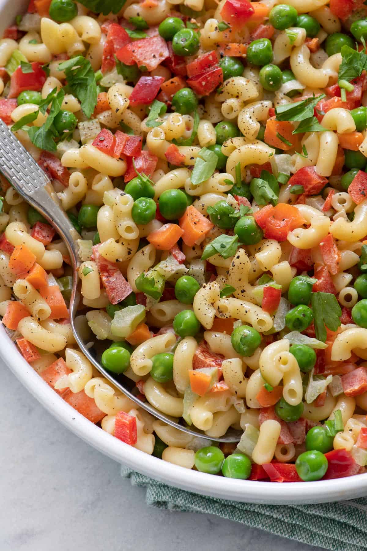 Close-up of recipe with spoon dipped in pasta with carrots, peas, celery and bell pepper.