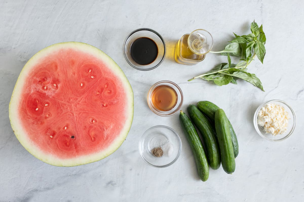 Ingredients for recipe: half watermelon, dressing ingredients, 4 small cucumbers, fresh basil, and feta.