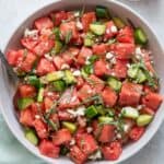 Cucumber watermelon salad in a large white serving bowl with a small glass bowl with extra chunks of watermelon.