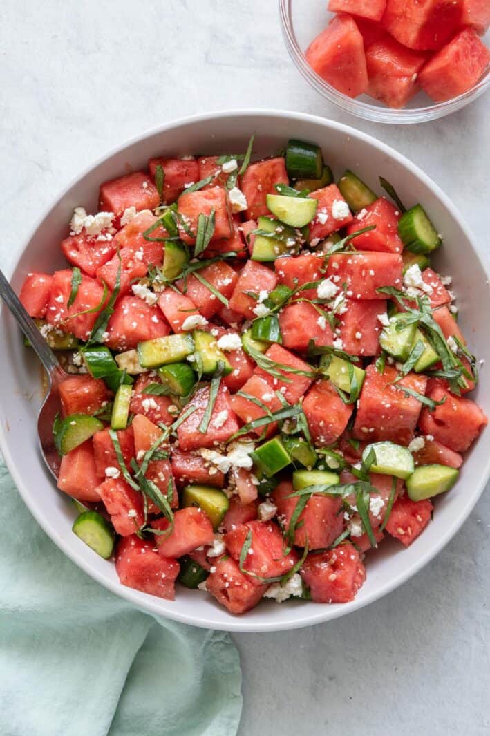 Cucumber watermelon salad in a large white serving bowl with a small glass bowl with extra chunks of watermelon.