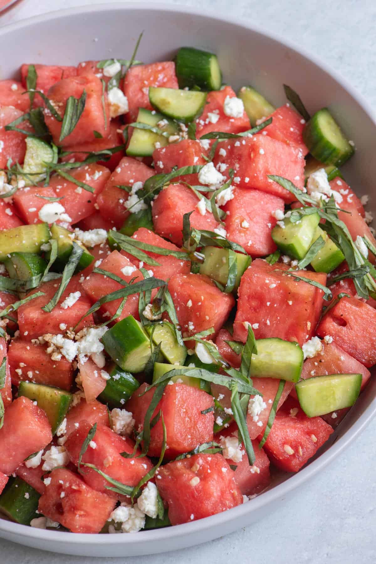 Close up of watermelon and cucumber salad in white bowl.