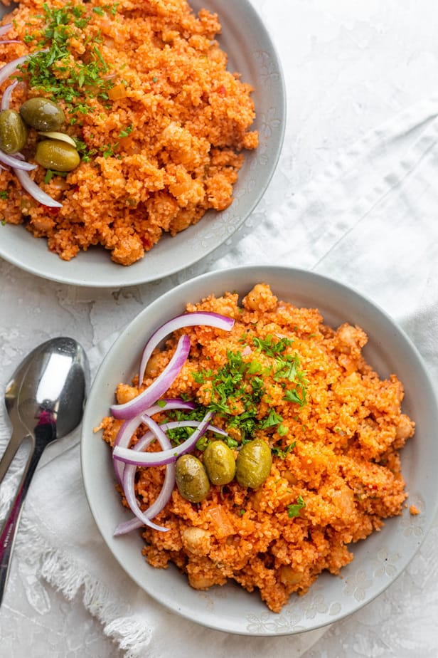 Two plates of bulgur pilaf topped with parsley, olives and onions