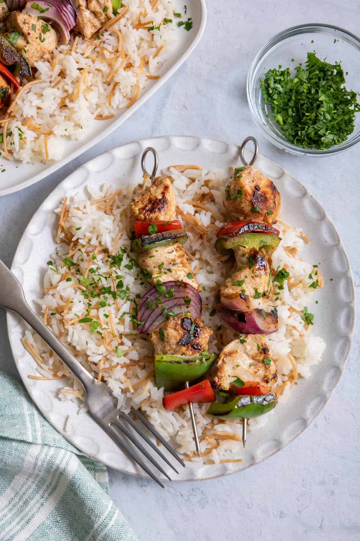 Two grilled chicken kabob skewers on a plate served over Lebanese rice with parsley on the side