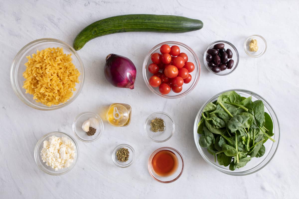 Ingredients for recipe: dry pasta, seasonings, cucumber, spinach, cherry tomatoes, black olives, feta cheese, red wine vinegar, and olive oil.