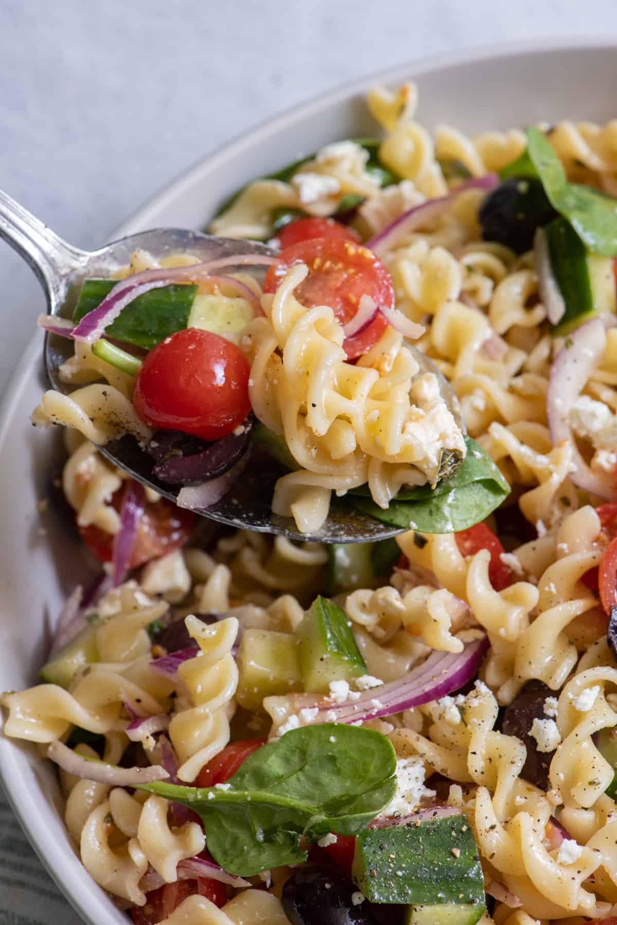 Side shot of spoon in pasta salad serving dish.