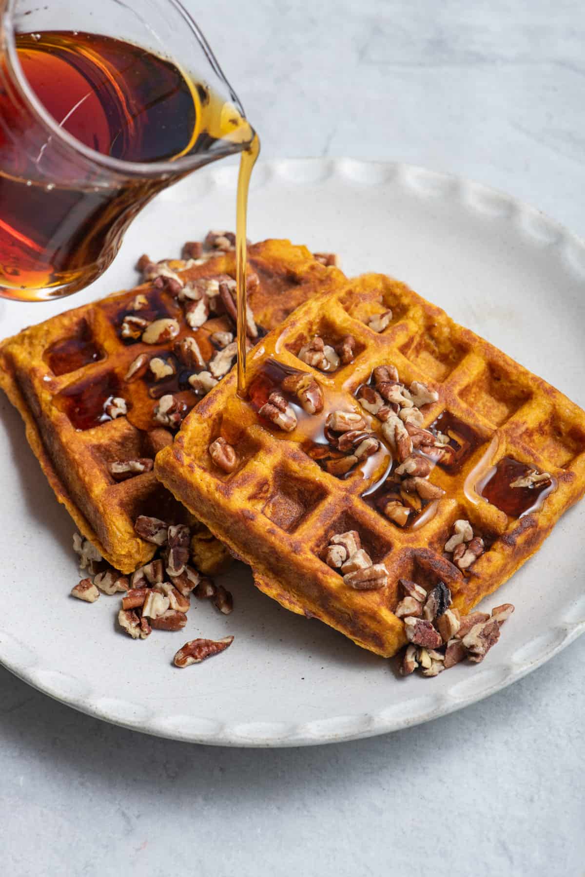Maple syrup getting poured on top of two sweet potato waffles