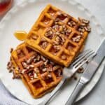 Sweet potato waffles stack on small white plate with fork and knife next to it.