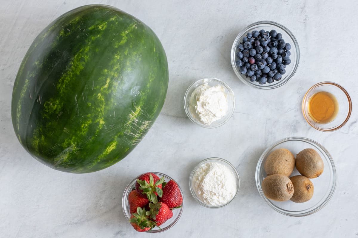 Ingredients for recipe: whole watermelon, strawberries, ricotta, whipped cream cheese, blueberries, whole kiwis, and honey.
