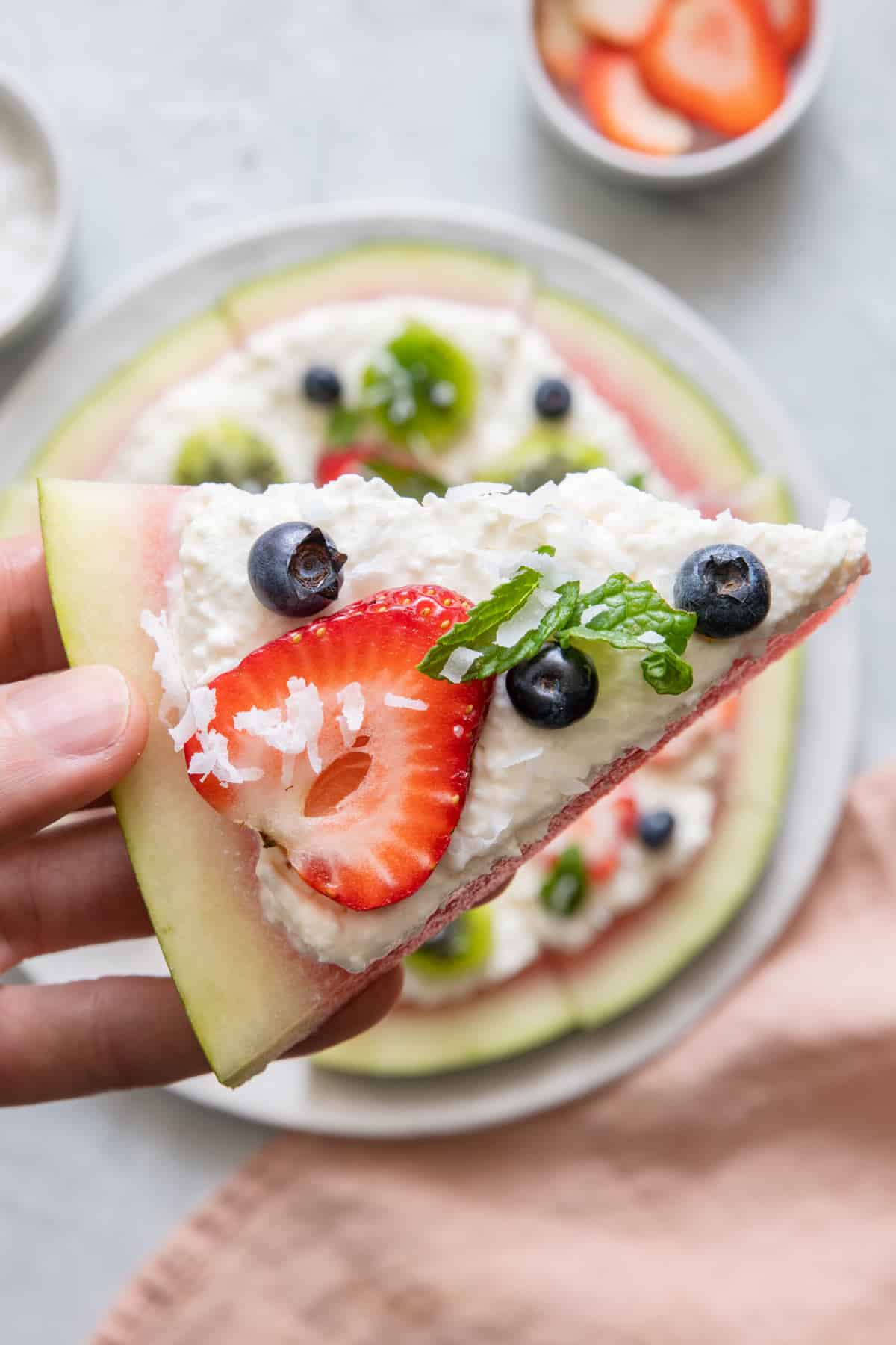 Close up shot of a slice of watermelon pizza with whole pizza show behind it.