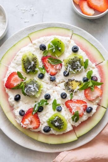 Watermelon pizza on large white plate cut into 8 pieces.