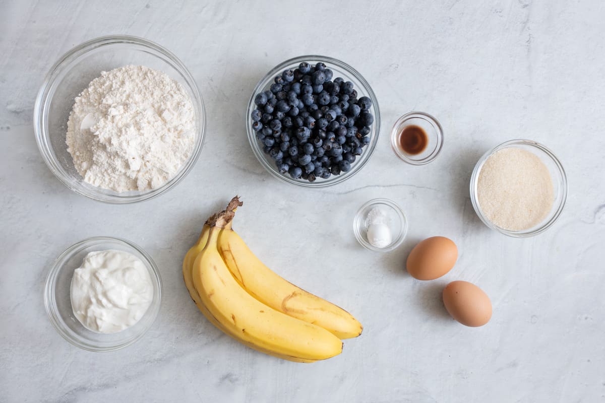 Ingredients for recipe: flour, yogurt, fresh blueberries, 3 bananas, vanilla, salt and baking powder, 2 brown eggs, and sugar.