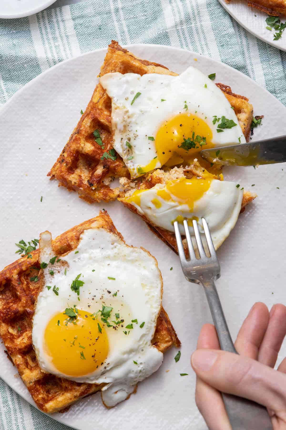 Fork and knife cutting into egg on top of cauliflower waffles