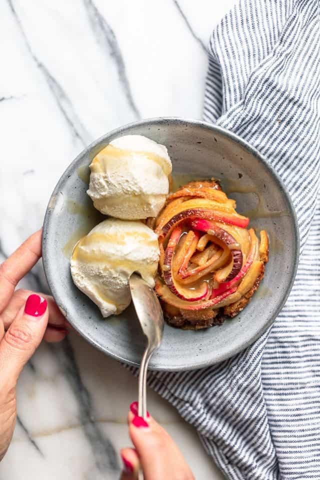 Final shot of the Rose Apple Pie with two scoops of vanilla ice cream and a spoon about to take a bite.