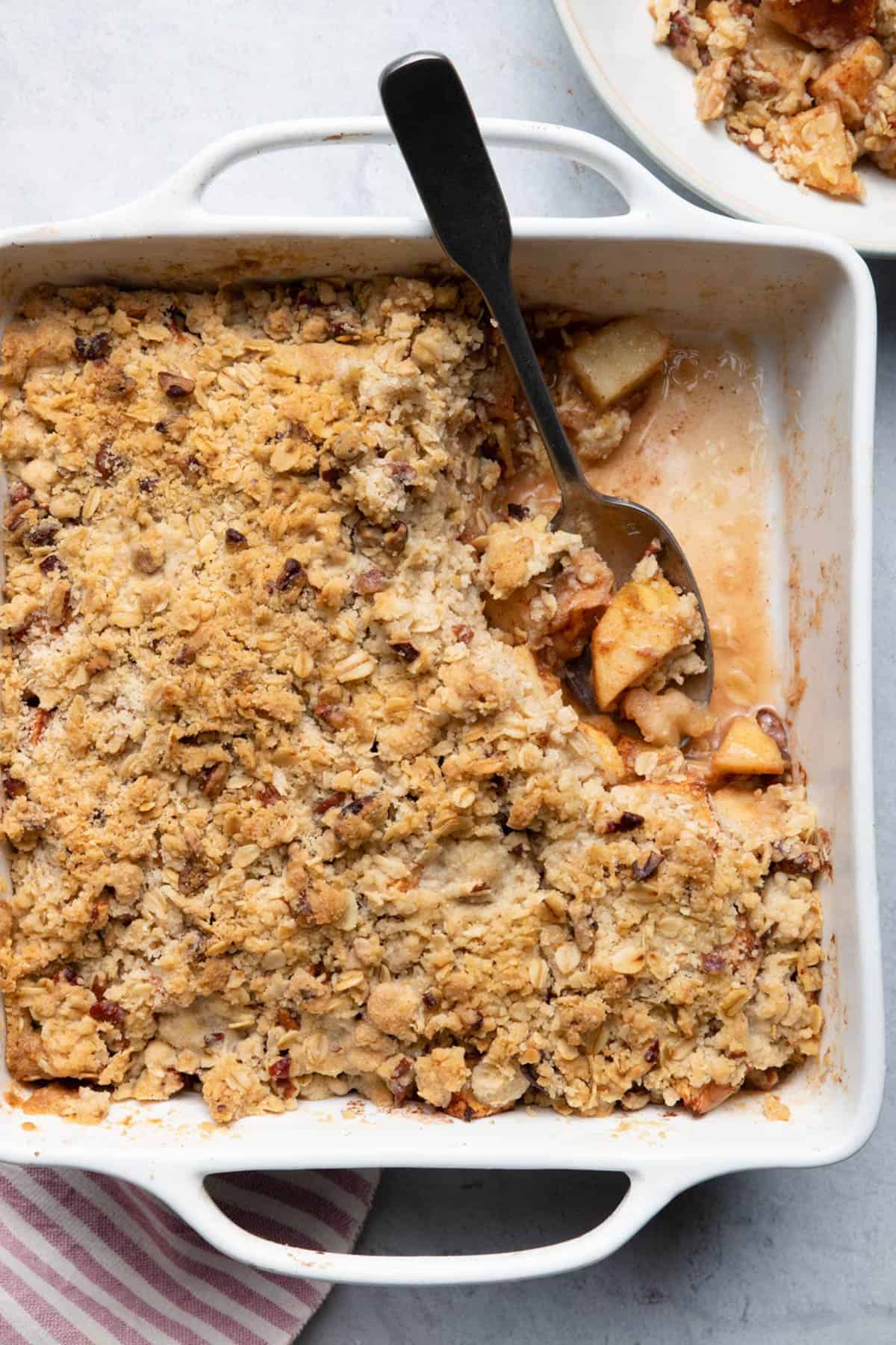 Easy apple crisp out of the oven in a white baking dish with spoon inside