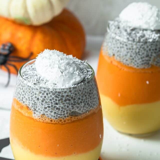 Final shot of candy corn parfait layered in a clear glass with pumpkin in background and halloween decorations
