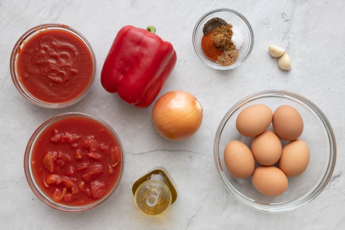 Ingredients for recipe: tomato sauce, diced tomatoes, red bell pepper, yellow onion, oil, spices, garlic cloves, and eggs.