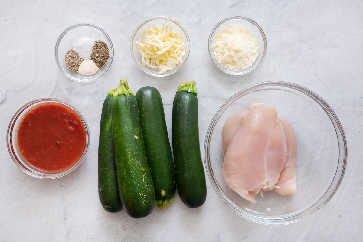 Ingredients for recipe before being prepped: seasonings, marinara, shredded cheese, zucchinis, parmesan cheese, and chicken breasts.