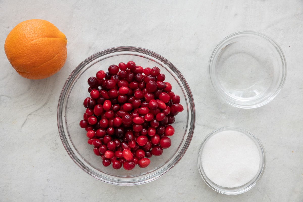 Ingredients for recipe in individual bowls: 1 orange, fresh cranberries, water, and sugar.